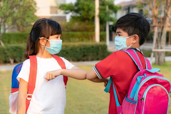 Elbow bump is new novel greeting to avoid the spread of coronavirus. Two Asian children preschool friends meet in  school park with bare hands. Instead of greeting with a hug or handshake, they bump elbows instead.