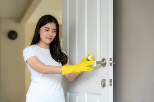 Normal shot of a Asian woman disinfecting the door knobs by spraying a blue sanitizer from a bottle. Prevent the virus and bacterias, Prevent covid19, corona virus, Alcohol Sanitizer.Hygiene concept at home.