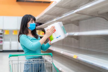 Asian woman looking at Supermarket empty toilet paper shelves amid COVID-19 coronavirus fears, shoppers panic buying and stockpiling toilet paper preparing for a pandemic. clipart