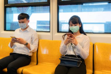 Metroda diğer insanlardan bir koltuk için maske takan iki Asyalı insan COVID-19 virüslerinden ve enfeksiyon riski ve hastalık önleme tedbirleri için sosyal mesafeyi koruyorlar.