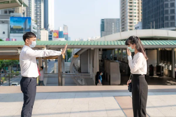 Asian ill businesswoman cough with mask and businessman stop sign hand him to keep distance protect from COVID-19 viruses and people social distancing for infection risk and disease prevention measures