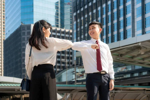 Elbow bump is new novel greeting to avoid the spread of coronavirus. Two Asian business friends meet in front of office building. Instead of greeting with a hug or handshake, they bump elbows instead.