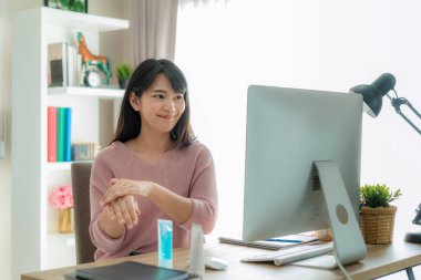 Alkol antiseptik jel kullanan Asyalı bir kadın sık sık ellerini temizler, enfeksiyonu önler, Covid-19 salgını dezenfektanla el yıkarken aynı zamanda evdeki sosyal mesafeyi bilgisayarla kapatır.