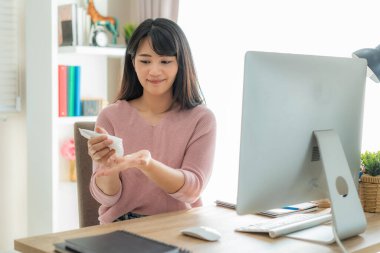 Korunmak için losyon ya da nemlendirici kullanan Asyalı bir kadın, evdeki sosyal mesafesinde bilgisayar kullanırken alkollü antiseptik jel kullandıktan sonra kuru ve tahriş olmuş ciltlerini korumak için günlük yaşamlarının bir parçası haline gelir.