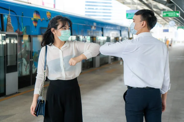 Elbow bump is new novel greeting to avoid the spread of coronavirus. Two Asian business friends meet in subway station. Instead of greeting with a hug or handshake, they bump elbows instead.