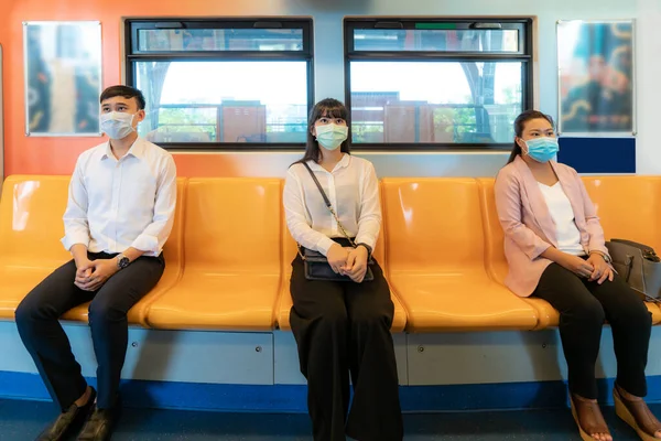 Three Asian people wearing mask sitting in subway distance for one seat from other people keep distance protect from COVID-19 viruses and people social distancing  for infection risk and disease prevention measures