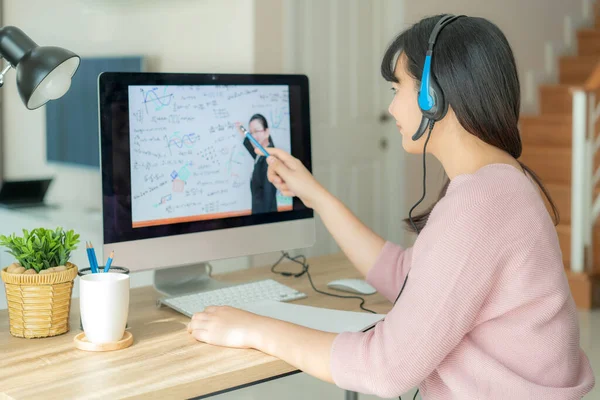 Asyalı kadın öğrenci video konferansında öğretmenle evde bilgisayar başında e-öğrenme. E-öğrenme, çevrimiçi, eğitim ve İnternet sosyal mesafesi COVID-19 virüslerinden koruma.
