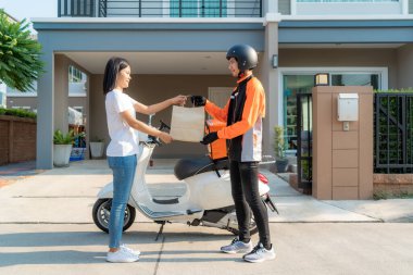 Scooter 'lı Asyalı bir kurye turuncu üniformalı bir gülümseme içinde yemek dağıtıyor, elinde yemek çantası tutuyor ve Asyalı bir kadın teslimatçıdan gelen çantayı kabul ediyor..