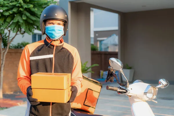 スクーター付きフロントハウス村の段ボール箱のオレンジ均一な保持杭に保護マスクを持つアジアの配信若い男 ビジネス 交通の概念 — ストック写真