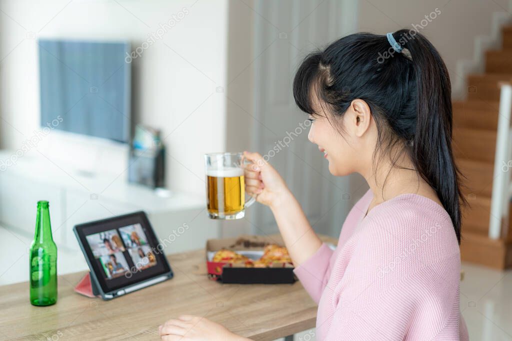 Asian woman virtual happy hour meeting party and drinking alcohol beer online together with her friend in video conference with digital tablet for a online meeting in video call for social distancing for infection risk.