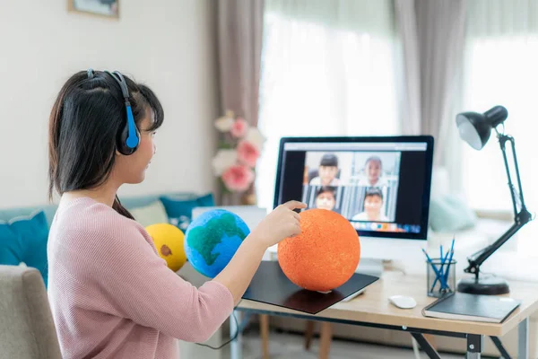 Asyalı kadın öğretmen video konferansında e-öğrenme ve neşeli ilkokul öğrencisi ile güneş sistemi öğretiyor. Dünya, ev eğitimi ve uzaklık öğrenimi, çevrimiçi, eğitim ve İnternet 'e bakıyor.