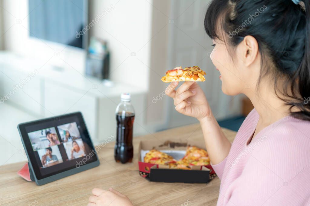 Asian woman virtual happy hour meeting party and eating food online together with her friend in video conference with digital tablet for a online meeting in video call for social distancing for infection risk.