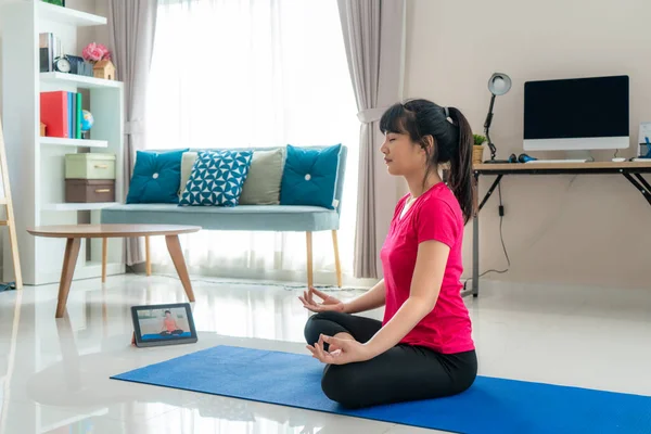 Asian woman making yoga exercise for step away from their computers to take mid-day exercise breaks via livestream videos classes on digital tablets during working from home.