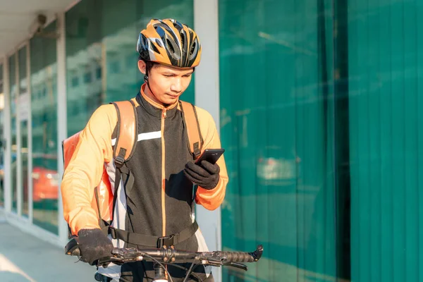 アジア人男性宅配便は お客様の住所を地図上で確認しますスマートフォン自転車で街中の食べ物を配達します — ストック写真