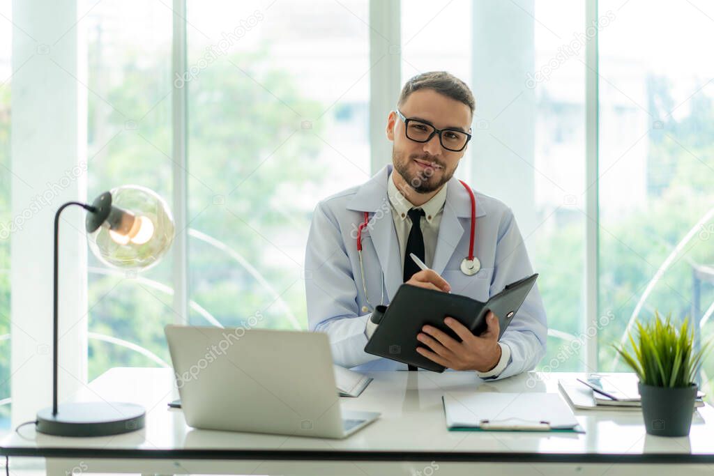 Doctor man sitting at the desk at his working place and smiling at camera. Perfect medical service in clinic. Happy future of medicine and healthcare. Happy doctor looking at camer