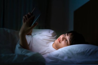 Asyalı mobil bağımlı kadın internette film veya sanal görüşme videosu izlemek için dijital tablet kullanıyor. Geceleri uyumadan önce erkek arkadaşıyla yatıyormuş.