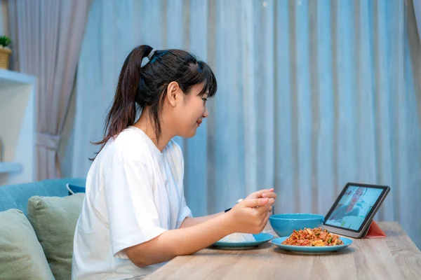 Asian woman virtual happy hour meeting dinner and eating food online together with her boyfriend in video conference with digital tablet for a online meeting in video call for social distancin