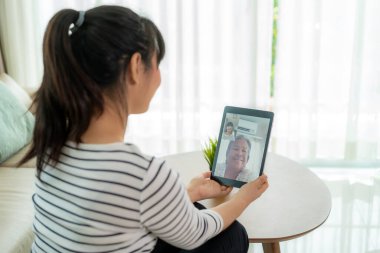 Asyalı genç bir kadın sanal mutlu saat buluşması ve dijital tabletle görüntülü bir konferansta annesiyle sosyal uzaklık için bir video görüşmesi yapıyor.