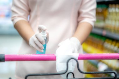 Coronavirus pandemik Covid-19 sırasında alışveriş arabasının koluna sprey sprey sıkarak dezenfekte eden bir kadın.