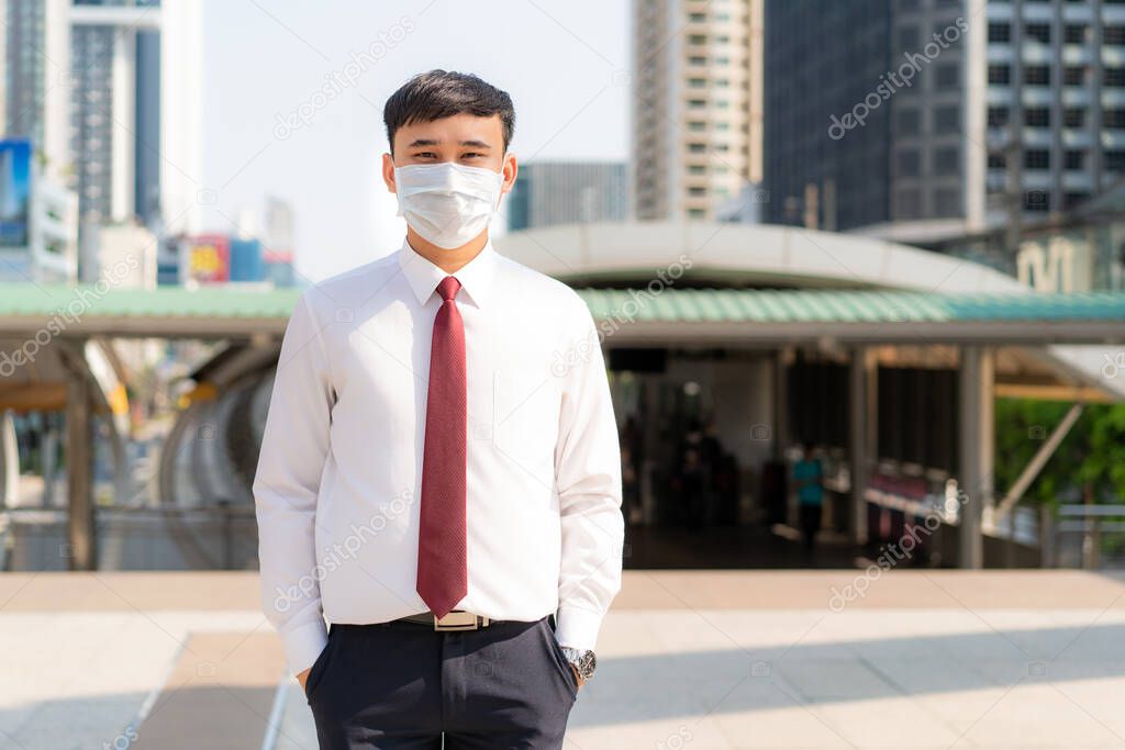 Young Asian businessman in white shirt going to work in pollution city she wears protection mask prevent PM2.5 dust, smog, air pollution and COVID-19 in Bangkok, Thailand.