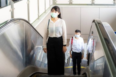Yüz maskesi takan iki Asyalı ve COVID-19 virüsünden korunmak için 2 metre mesafede. Bangkok, Tayland 'daki metro istasyonunda yürüyen merdivende enfeksiyon riski var..