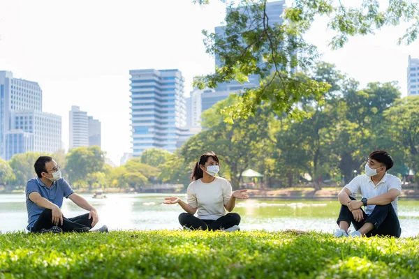 亚洲3名年轻男女和他们的朋友聊天和放松 戴着面具 坐在6英尺远的地方 保护他们免受Covid 19病毒的感染 以避免公园内的感染风险 — 图库照片