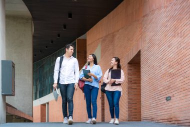 Üniversitede tatilde Asyalı üç öğrenci birlikte yürüyüp konuşuyor. Eğitim, Öğrenim, Öğrenci, Kampüs, Üniversite, Yaşam Tarzı Konsepti