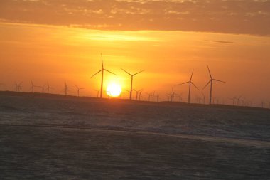 Rio Grande do Norte Brazil 'deki Galinhos yarımadasında arka planda elektrik üretmek için yel değirmenleriyle gün batımı manzarası