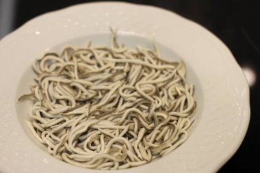 Beyaz tabakta sarımsaklı bebek yılan balıkları.