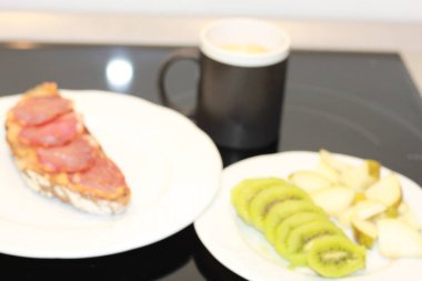 Sağlıklı ve lezzetli kahvaltı, dilimlenmiş meyve, doğal domatesli çavdar ekmeği tost ve İber filetosu ve sütlü kahve.