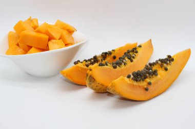 Beyaz arka planda bir kase papaya küpünün yanında yeni kesilmiş papaya parçaları.