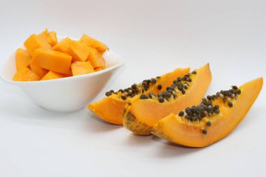 Beyaz arka planda bir kase papaya küpünün yanında yeni kesilmiş papaya parçaları.
