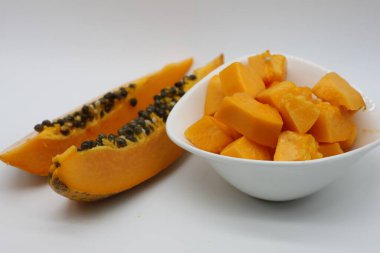 Beyaz arka planda bir kase papaya küpünün yanında yeni kesilmiş papaya parçaları.