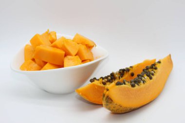 Beyaz arka planda bir kase papaya küpünün yanında yeni kesilmiş papaya parçaları.