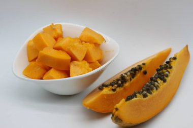 Beyaz arka planda bir kase papaya küpünün yanında yeni kesilmiş papaya parçaları.