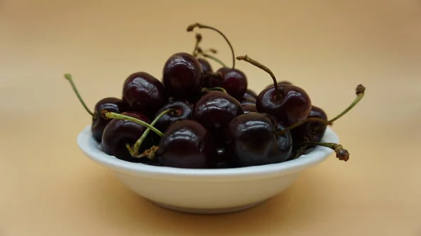red cherries in a white bowl on salmon background