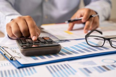 İş adamı, hesap makinesi strateji analizi kullanarak finansal belge veri grafiklerini analiz etmeyi planlıyor.