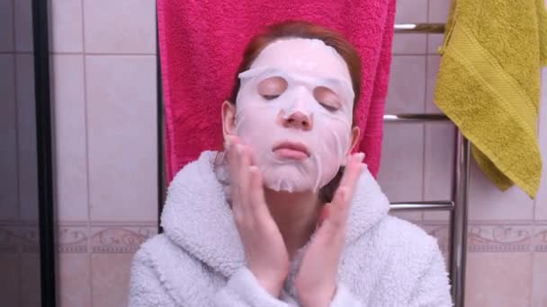 Mulher está aplicando máscara de folha em seu rosto no banheiro — Vídeo de Stock