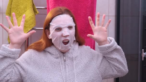 Kvinnan med en kosmetisk mask i ansiktet skrämmer sig själv. Kul med en mask i ansiktet. — Stockvideo