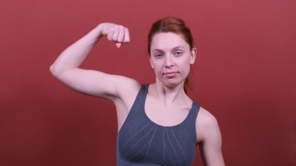 Μια νεαρή αθλητική γυναίκα με κόκκινα μαλλιά αναδεικνύει τους δικέφαλους της. Ο αθλητισμός είναι καλός — Αρχείο Βίντεο