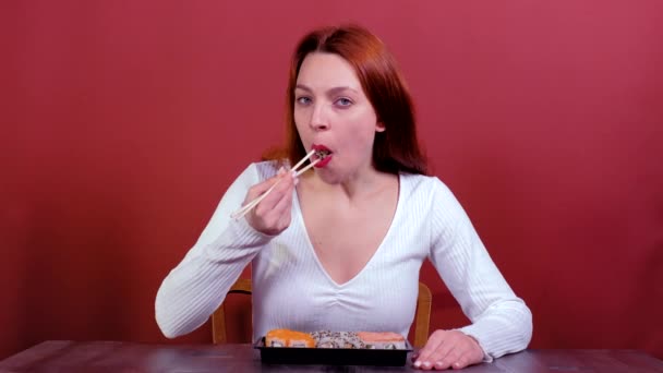 Piękna kobieta jedząca sushi na czerwonym tle. — Wideo stockowe