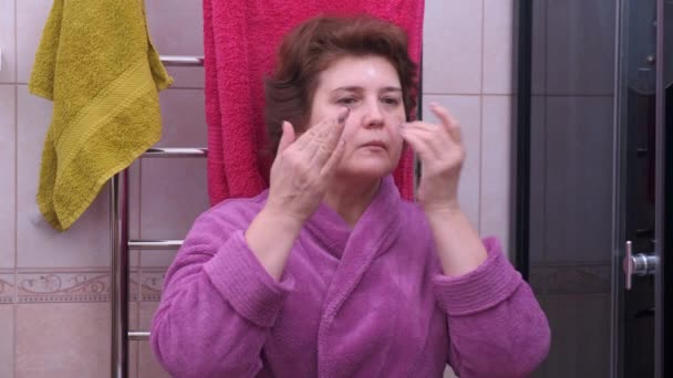 Mulher de meia-idade aplicando creme facial em seu rosto — Vídeo de Stock