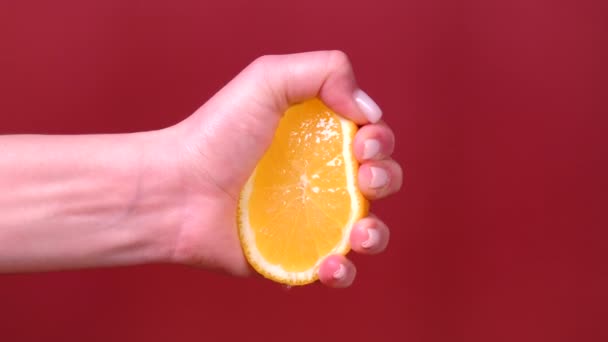 Kvinnlig hand klämmer orange isolerad på rött — Stockvideo