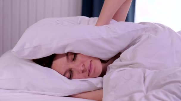 Jonge vrouw probeert te slapen geïrriteerd door slechte lawaaierige kamer buren bedekt oren met kussen, wakker worden liggend in bed lijden aan slapeloosheid — Stockvideo