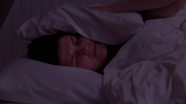 Wanita muda yang mencoba untuk tidur terganggu oleh kamar tetangga yang berisik menutupi telinga dengan bantal, bangun berbaring di tempat tidur menderita insomnia — Stok Video