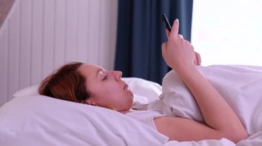 Kızıl saçlı kadın sabah uyanır ve akıllı telefonunu kullanmaya başlar.