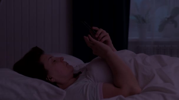 Ενήλικες γυναίκα ξαπλωμένη στο κρεβάτι τη νύχτα και χρησιμοποιώντας το smartphone της — Αρχείο Βίντεο