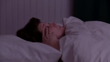 Yetişkin bir kadın beyaz bir yastığın üzerinde uyuyor. Uyanıyor ve gece gözlerini açıyor..