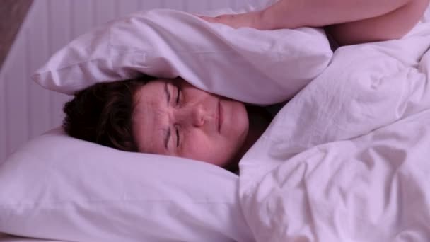 Женщина пытается спать раздраженный плохой шумные соседи комната покрывая уши подушкой, проснуться лежа в постели страдают от бессонницы — стоковое видео