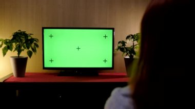 Oturma odasındaki bir kanepede oturan kadının 4K görüntüsü, yeşil ekranlı televizyon izliyor.